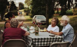 man in white crew neck t-shirt sitting on chair in front of table with food by leah hetteberg courtesy of Unsplash.