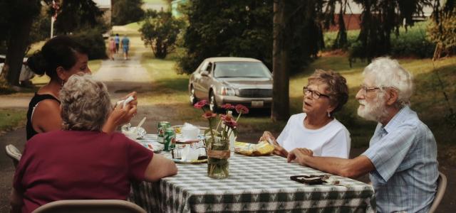 man in white crew neck t-shirt sitting on chair in front of table with food by leah hetteberg courtesy of Unsplash.